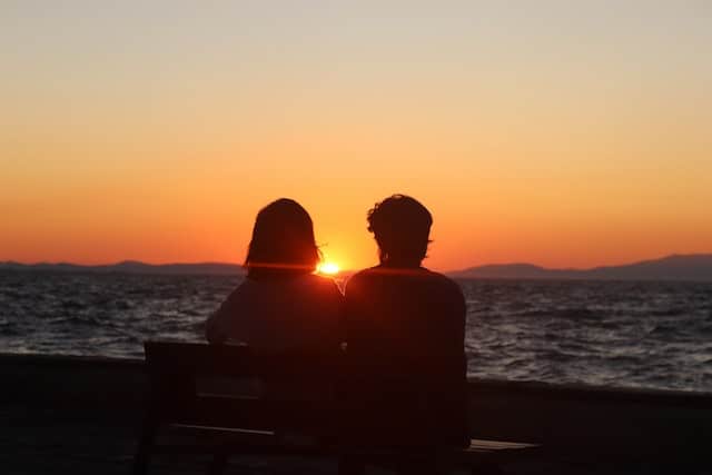 A couple sitting on a bench in front of sunset