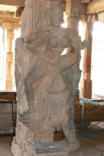 A stone Rati sculpture on a temple pillar, opposite the pillar with Kama. Seated on a parrot, Rati is holding a sugarcane bow.